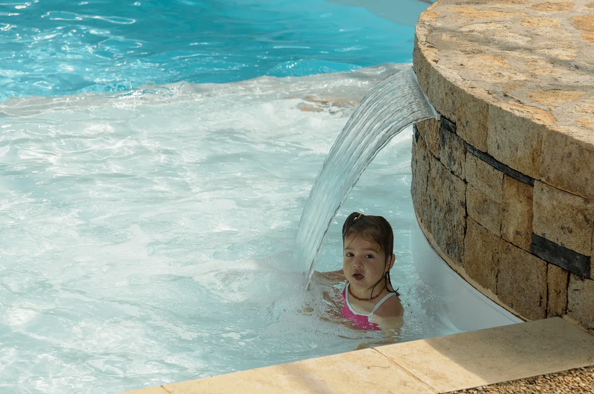 Enfant profitant d’un moment ludique sous une cascade d’eau dans la piscine du Domaine de Mesqueau à Plougasnou.