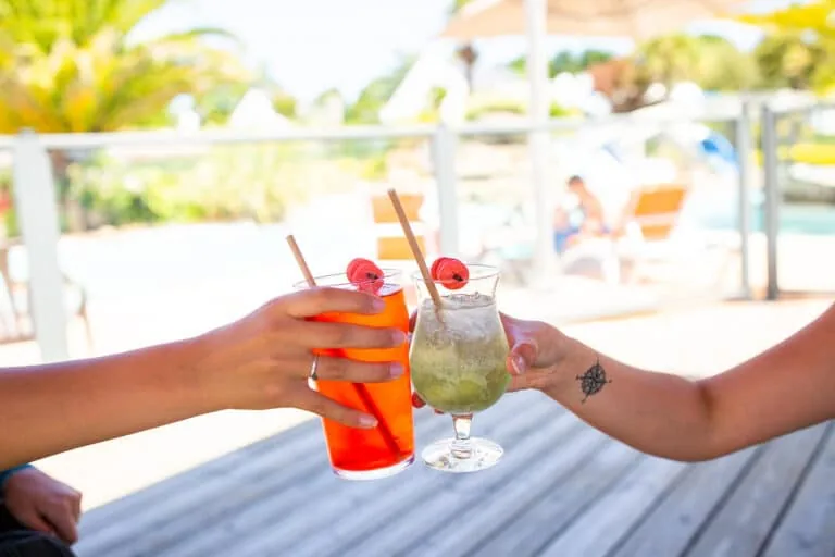 Deux personnes trinquent avec des cocktails rouges et verts agrémentés de cerises, dans un décor extérieur ensoleillé au bord de la piscine, rappelant une journée parfaite à Fouesnant.