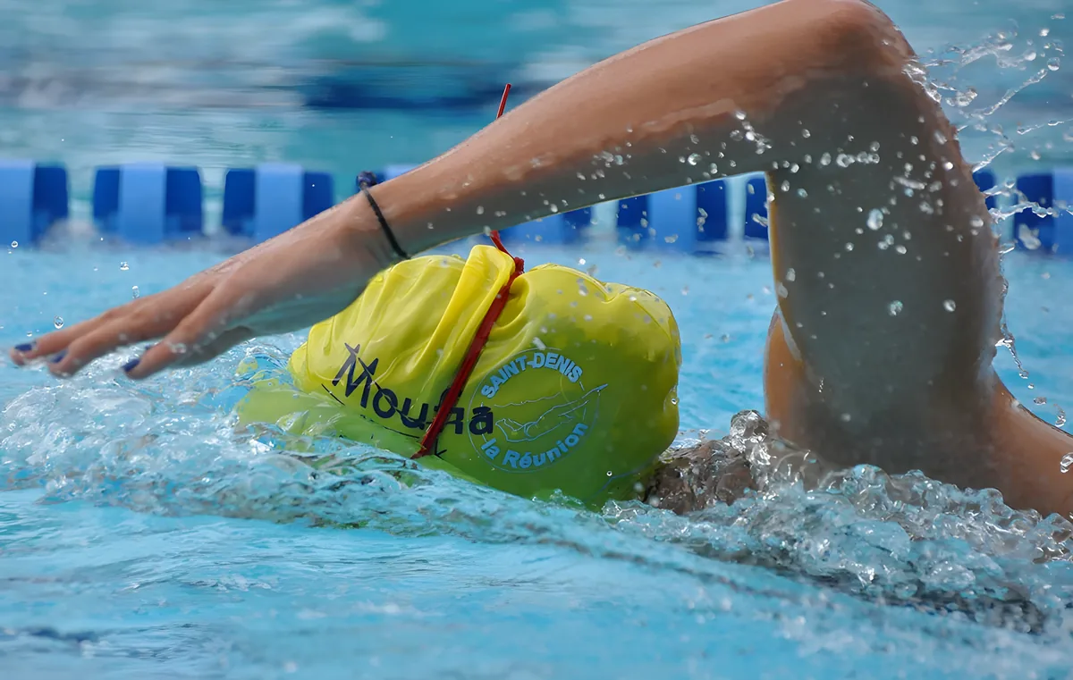 personne nageant dans piscine avec bonnet jaune sur lequel est inscrit le logo de Moufia Aquatik